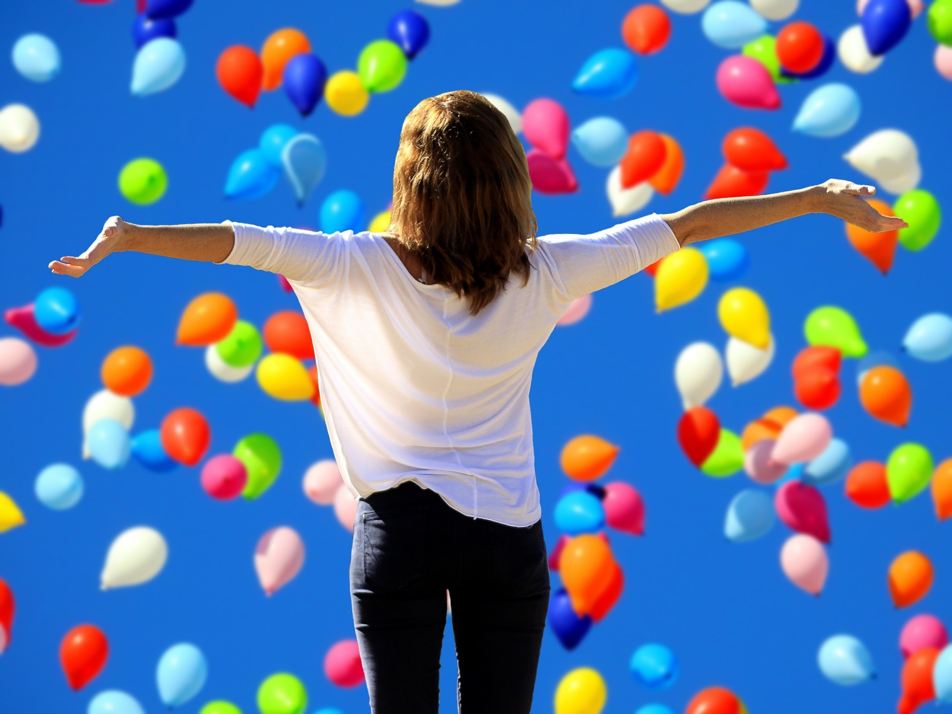 Woman with outstretched arms looking at falling balloons